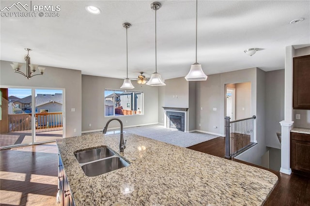 kitchen with an island with sink, light stone countertops, decorative light fixtures, and sink