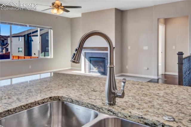 room details featuring ceiling fan, sink, light stone counters, and a tile fireplace