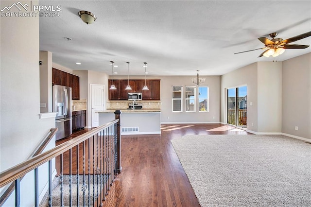 kitchen with backsplash, dark wood-type flooring, stainless steel appliances, hanging light fixtures, and an island with sink