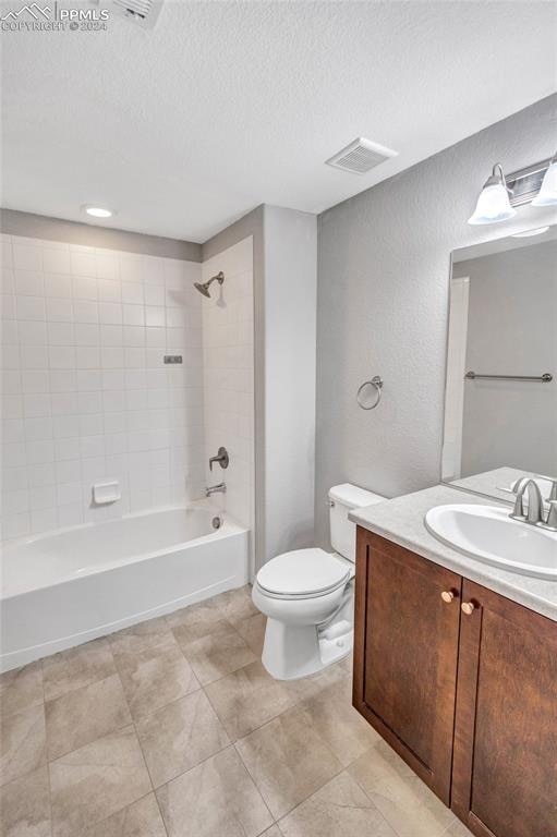 full bathroom with a textured ceiling, tiled shower / bath combo, vanity, and toilet