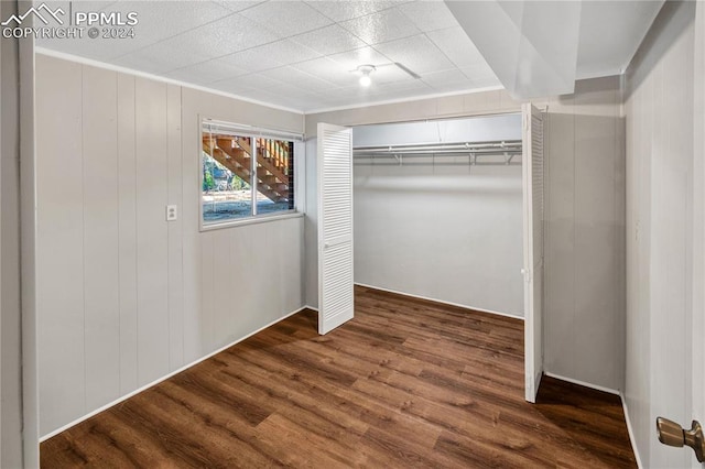 unfurnished bedroom with a closet, wooden walls, and dark hardwood / wood-style floors