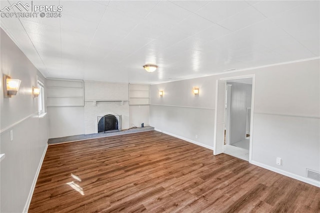 unfurnished living room featuring wood-type flooring, a fireplace, and built in shelves