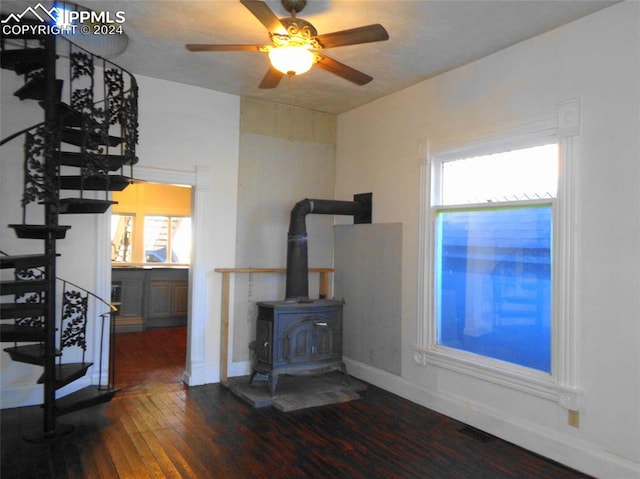 living room featuring dark hardwood / wood-style flooring, ceiling fan, and a wood stove