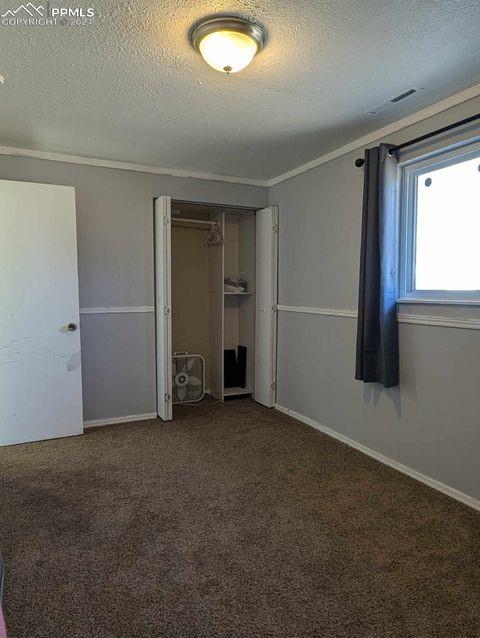 unfurnished bedroom with a closet, a textured ceiling, ornamental molding, and dark carpet