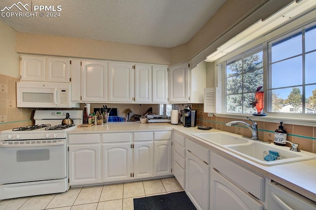 kitchen with white appliances, light tile patterned flooring, sink, white cabinets, and decorative backsplash