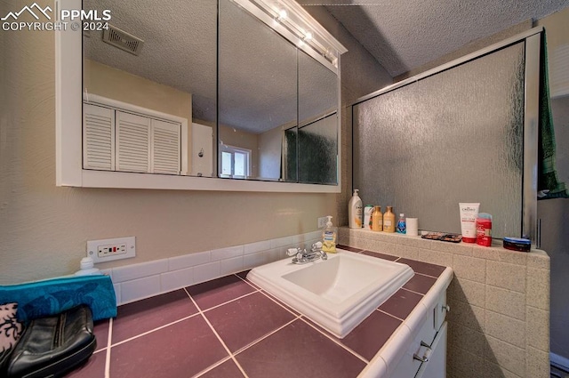 bathroom featuring vanity, tile patterned floors, a textured ceiling, and a shower with door