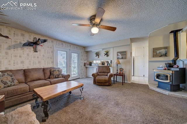 living room featuring french doors, a wood stove, a textured ceiling, ceiling fan, and carpet