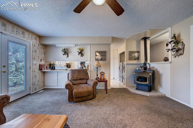 living room featuring light carpet, a textured ceiling, a wood stove, and ceiling fan