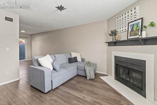 living room featuring a tile fireplace, wood-type flooring, and a textured ceiling