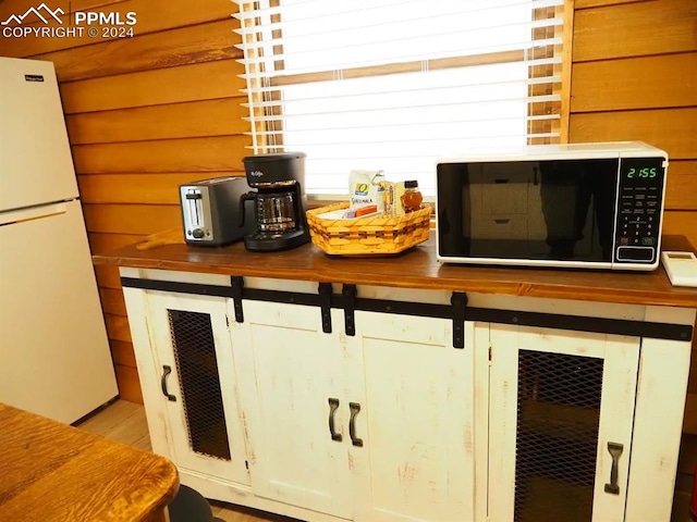 kitchen featuring wood walls, white cabinetry, butcher block counters, and white refrigerator