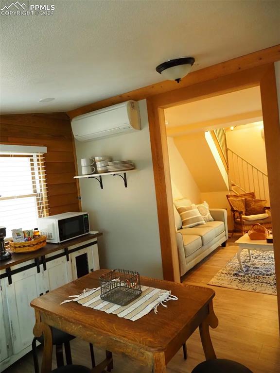 dining room with an AC wall unit, light hardwood / wood-style floors, and a textured ceiling