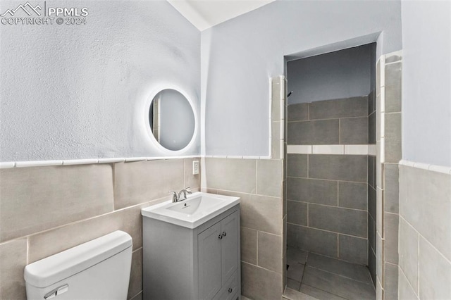 bathroom with a tile shower, vanity, tile walls, and toilet