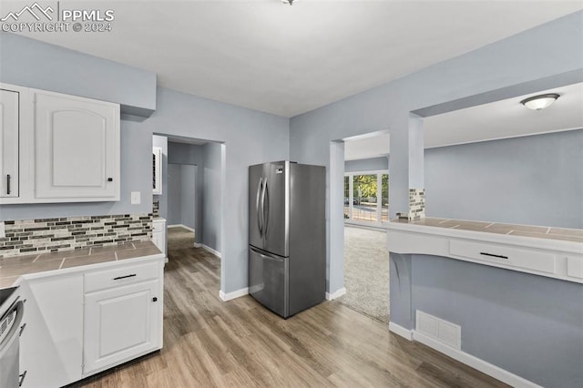 kitchen featuring stainless steel refrigerator, light wood-type flooring, tile countertops, backsplash, and white cabinets