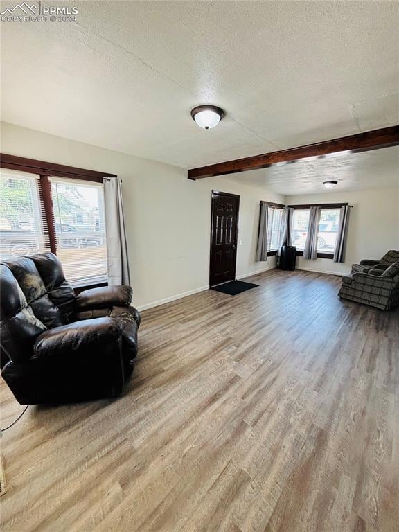 living room with beamed ceiling, a textured ceiling, and light wood-type flooring