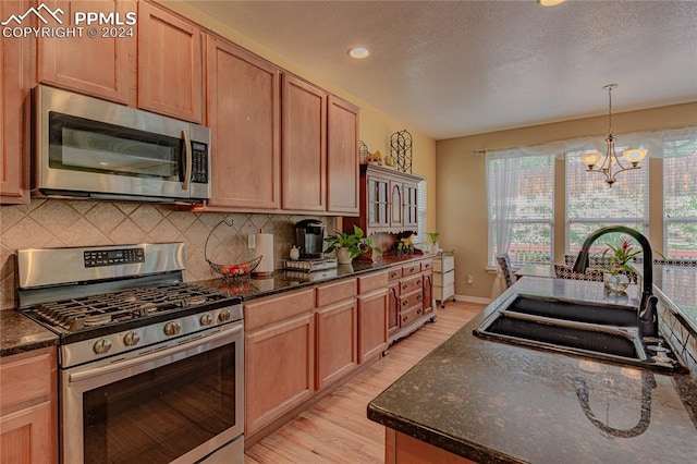 kitchen featuring sink, backsplash, stainless steel appliances, a notable chandelier, and light hardwood / wood-style floors