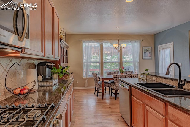 kitchen featuring light hardwood / wood-style floors, sink, an inviting chandelier, stainless steel appliances, and dark stone countertops