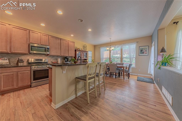 kitchen with light wood-type flooring, a kitchen island with sink, a kitchen bar, hanging light fixtures, and appliances with stainless steel finishes