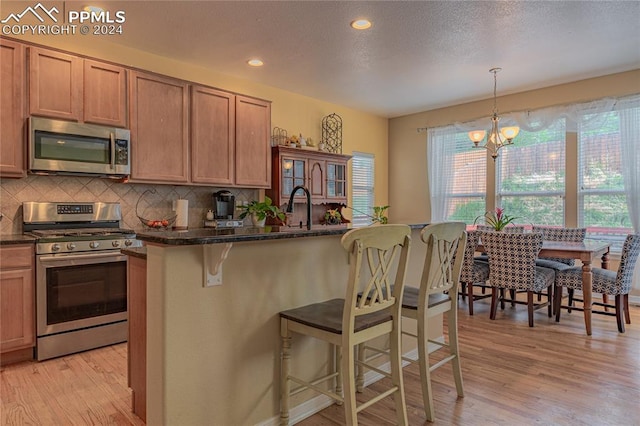 kitchen featuring light hardwood / wood-style floors, a breakfast bar area, a notable chandelier, appliances with stainless steel finishes, and decorative light fixtures