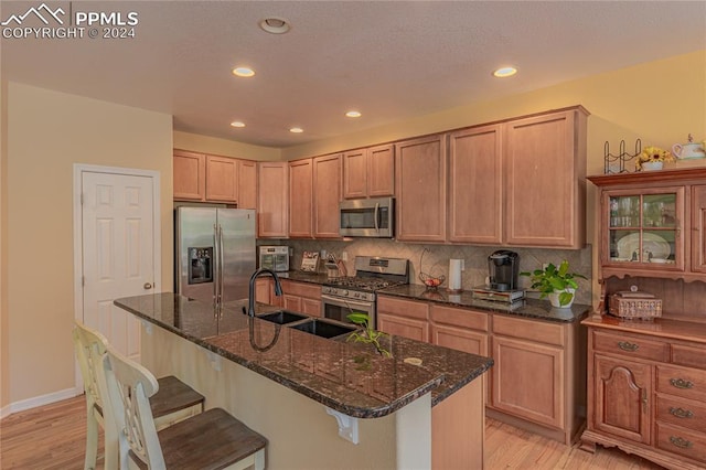 kitchen featuring stainless steel appliances, a breakfast bar, dark stone counters, light hardwood / wood-style floors, and decorative backsplash