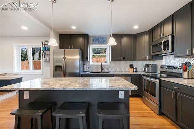 kitchen with decorative light fixtures, appliances with stainless steel finishes, sink, and light wood-type flooring