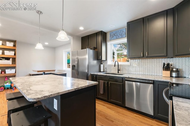 kitchen featuring light hardwood / wood-style flooring, decorative light fixtures, sink, stainless steel appliances, and a center island