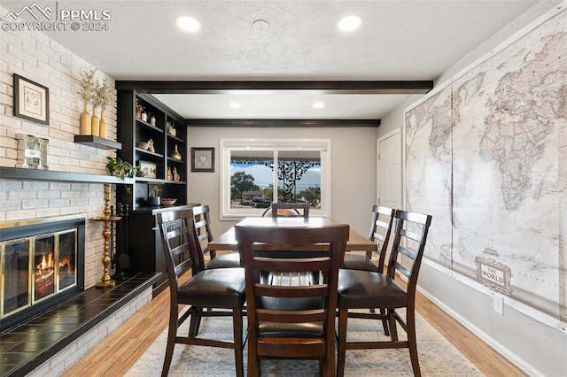 dining area featuring a fireplace, beam ceiling, wood-type flooring, and a textured ceiling