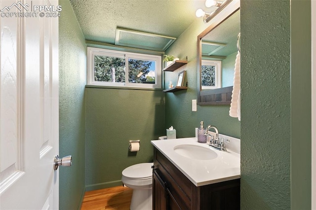 bathroom with a healthy amount of sunlight, toilet, wood-type flooring, vanity, and a textured ceiling