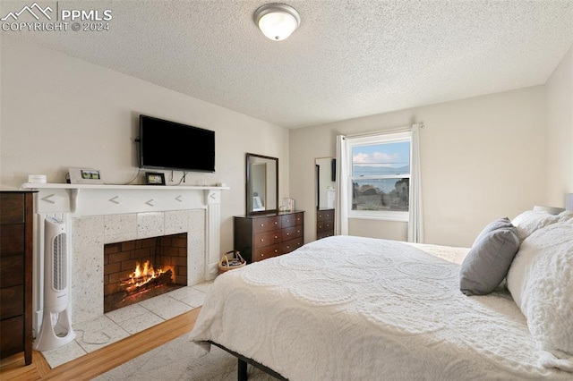 bedroom featuring light hardwood / wood-style flooring, a textured ceiling, and a tiled fireplace