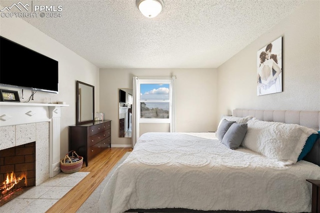 bedroom with a textured ceiling, a fireplace, and light hardwood / wood-style floors