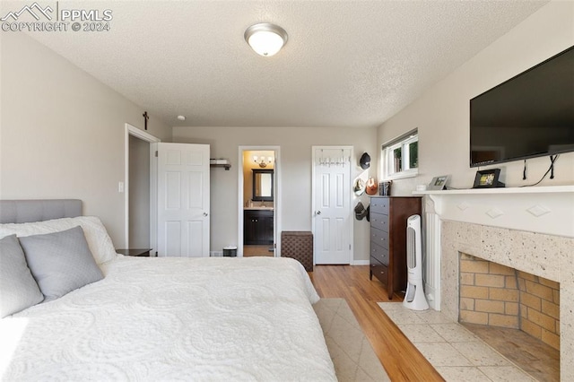 bedroom with a textured ceiling, light wood-type flooring, a fireplace, and ensuite bathroom