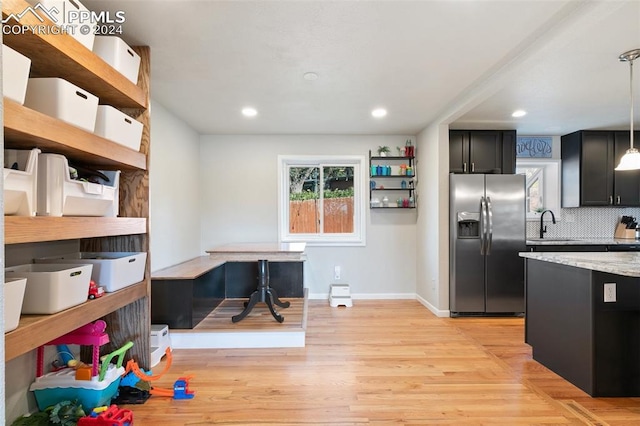 kitchen featuring pendant lighting, light hardwood / wood-style flooring, light stone counters, backsplash, and stainless steel refrigerator with ice dispenser