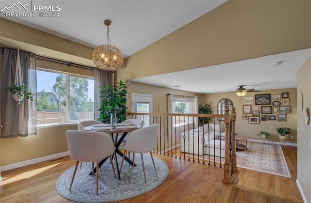 dining room with ceiling fan with notable chandelier, light hardwood / wood-style flooring, and vaulted ceiling