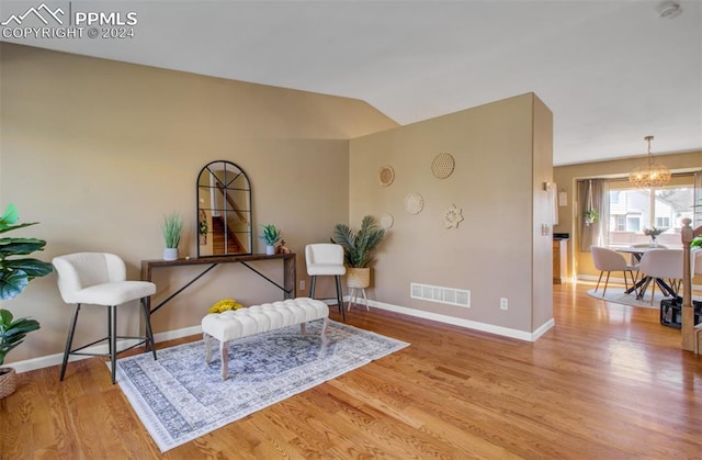 living area with an inviting chandelier, lofted ceiling, and light hardwood / wood-style floors