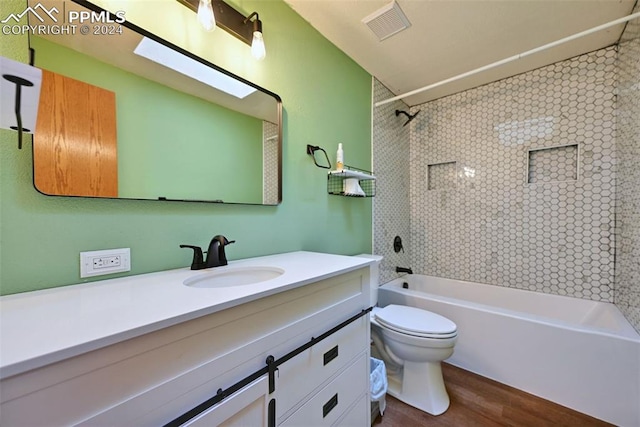 full bathroom featuring a skylight, toilet, tiled shower / bath, hardwood / wood-style flooring, and vanity