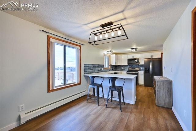 kitchen with kitchen peninsula, dark wood-type flooring, a baseboard heating unit, white cabinetry, and stainless steel appliances