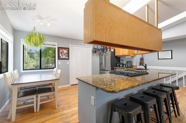 kitchen featuring dark stone counters, light wood-type flooring, a kitchen breakfast bar, and stainless steel fridge with ice dispenser