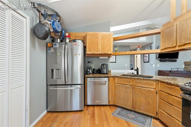 kitchen with appliances with stainless steel finishes, lofted ceiling, sink, and light hardwood / wood-style flooring