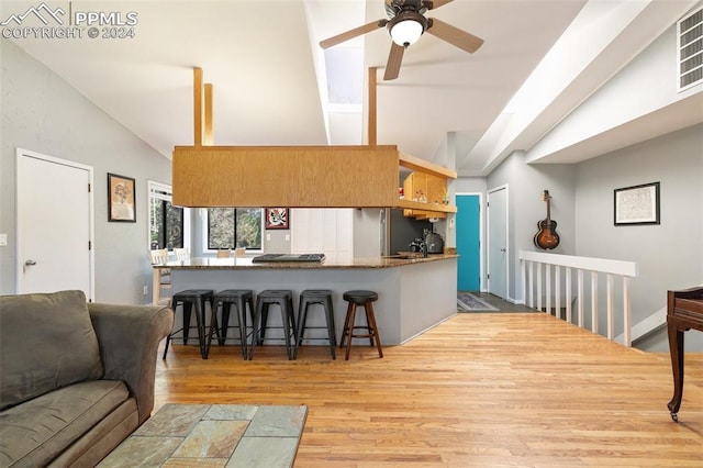 kitchen featuring kitchen peninsula, a breakfast bar area, light wood-type flooring, vaulted ceiling with skylight, and ceiling fan