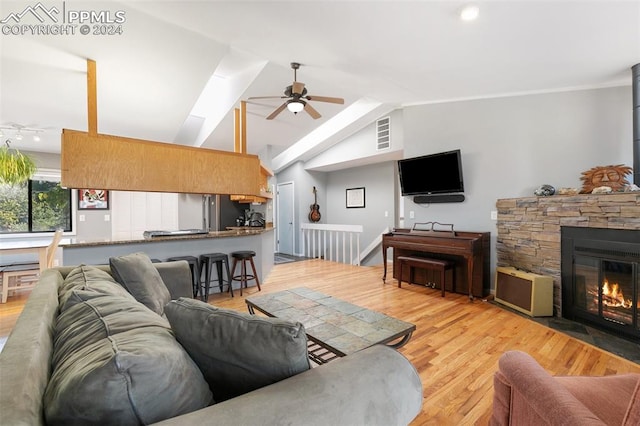 living room with ceiling fan, light hardwood / wood-style floors, a fireplace, and lofted ceiling with skylight