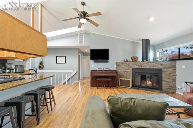 living room featuring ceiling fan, light hardwood / wood-style floors, sink, a stone fireplace, and vaulted ceiling