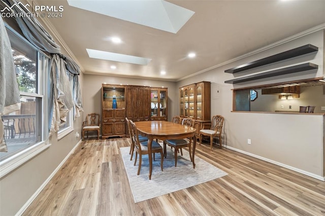 dining area with a skylight, crown molding, and light hardwood / wood-style floors