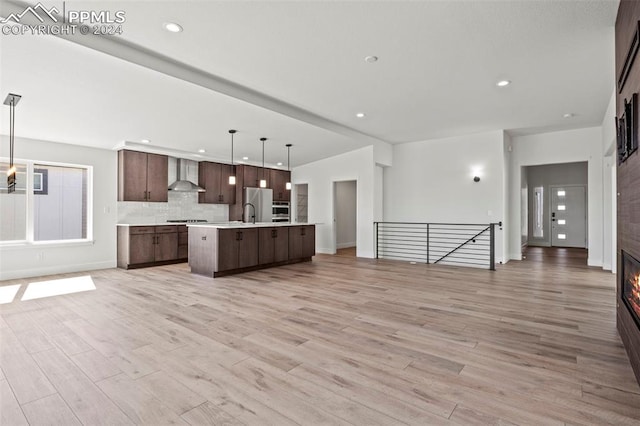 kitchen featuring an island with sink, pendant lighting, wall chimney exhaust hood, and light hardwood / wood-style flooring