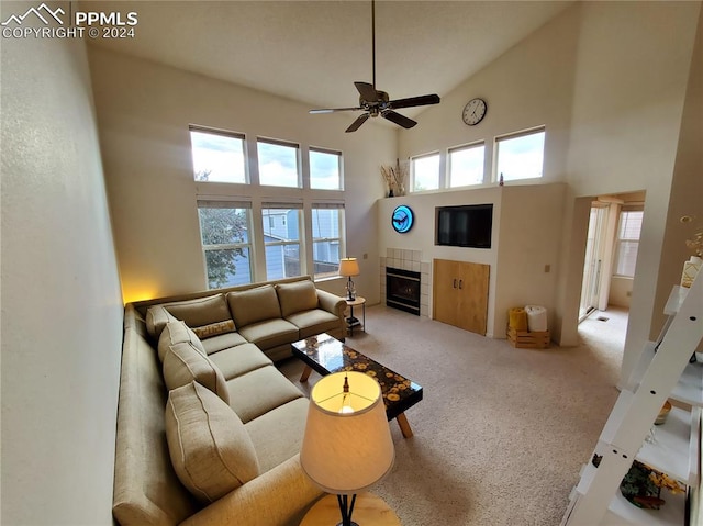 carpeted living room with ceiling fan, a tiled fireplace, and high vaulted ceiling