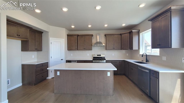 kitchen featuring light wood-type flooring, a center island, sink, wall chimney range hood, and appliances with stainless steel finishes