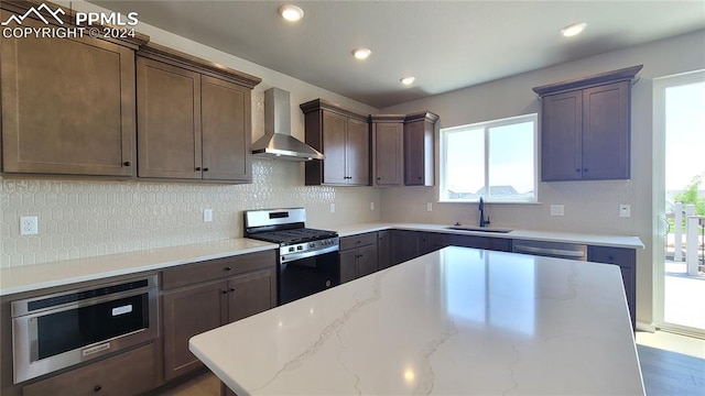 kitchen featuring appliances with stainless steel finishes, wall chimney range hood, decorative backsplash, and sink