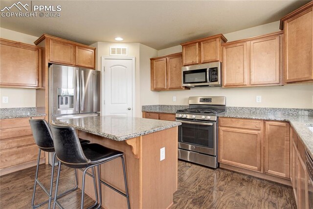 kitchen with appliances with stainless steel finishes, a kitchen island, light stone counters, a breakfast bar area, and dark hardwood / wood-style floors