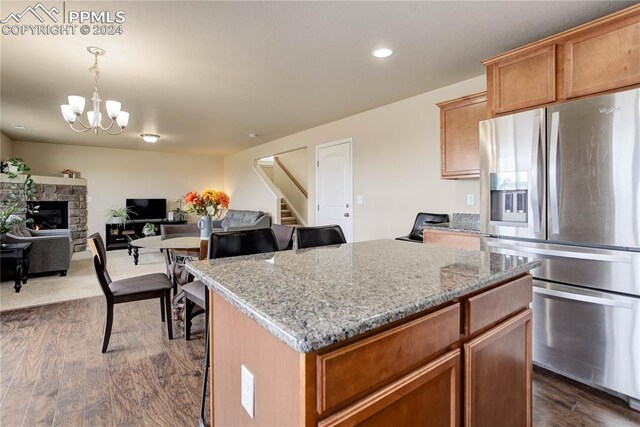 kitchen with decorative light fixtures, dark hardwood / wood-style flooring, a stone fireplace, stainless steel refrigerator with ice dispenser, and a center island