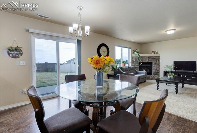 dining room featuring a stone fireplace, a chandelier, and wood-type flooring