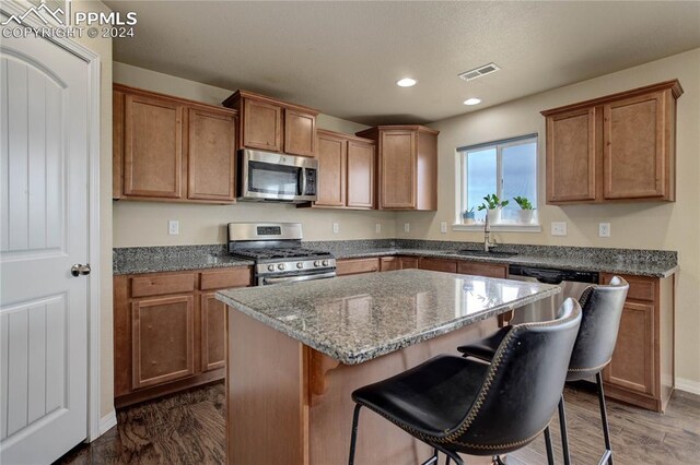 kitchen with a kitchen island, stone countertops, sink, appliances with stainless steel finishes, and dark hardwood / wood-style flooring