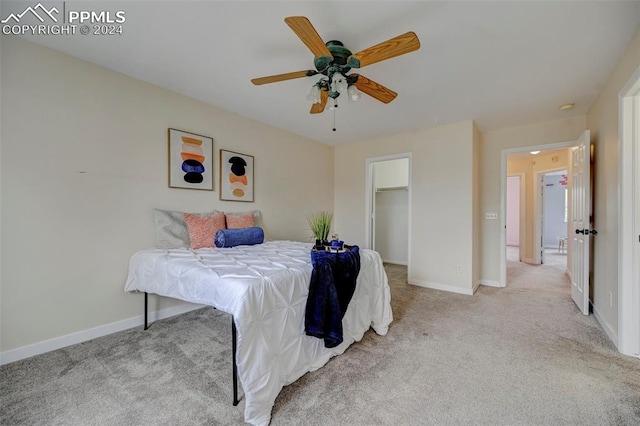 bedroom featuring a walk in closet, light colored carpet, a closet, and ceiling fan